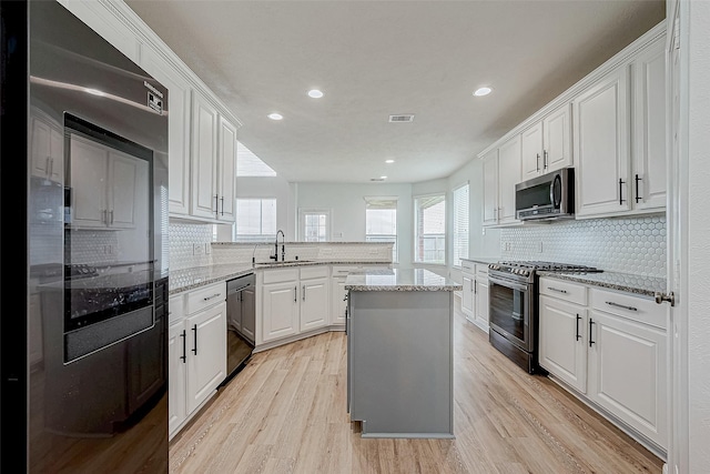 kitchen featuring light wood-style flooring, stainless steel appliances, a peninsula, a sink, and visible vents