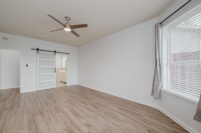 unfurnished bedroom featuring connected bathroom, light wood-style flooring, baseboards, and a barn door