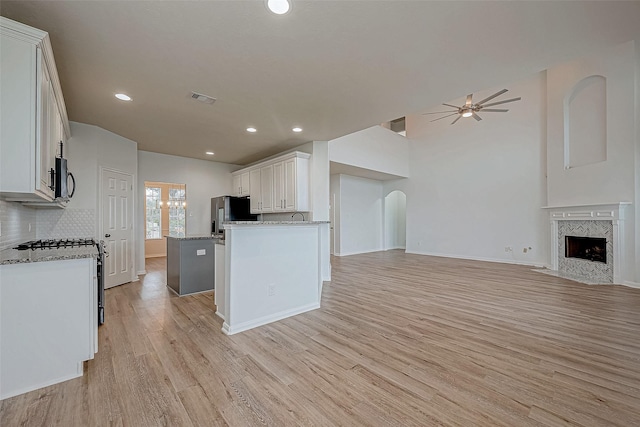 kitchen with light wood finished floors, a ceiling fan, open floor plan, stainless steel appliances, and a fireplace