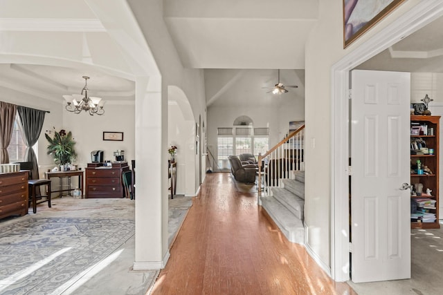 entrance foyer featuring arched walkways, stairway, a towering ceiling, wood finished floors, and ceiling fan with notable chandelier