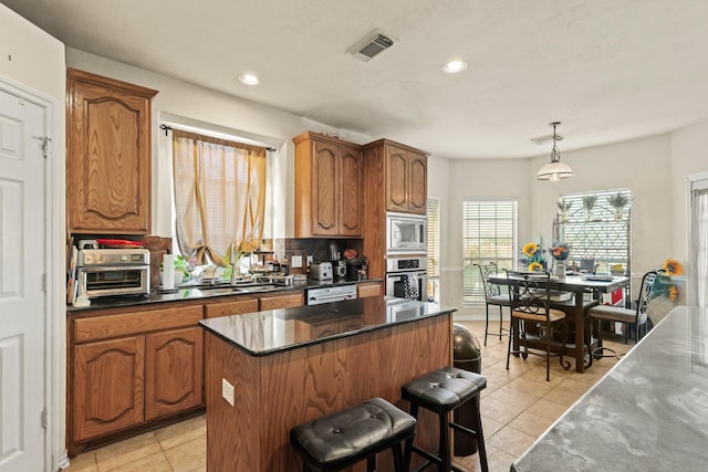 kitchen with a center island, brown cabinets, decorative light fixtures, stainless steel appliances, and tasteful backsplash