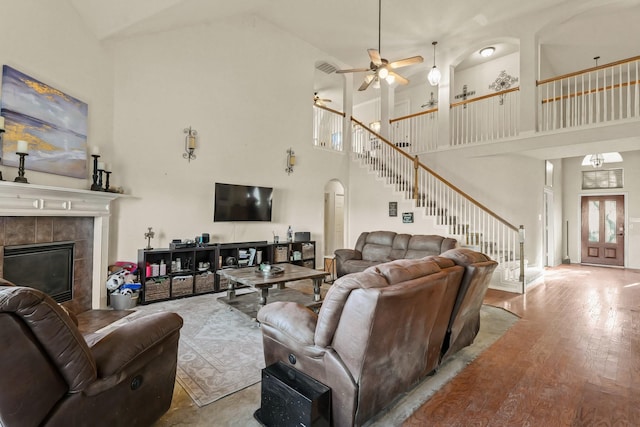 living area featuring arched walkways, stairway, a high ceiling, light wood-style floors, and a fireplace