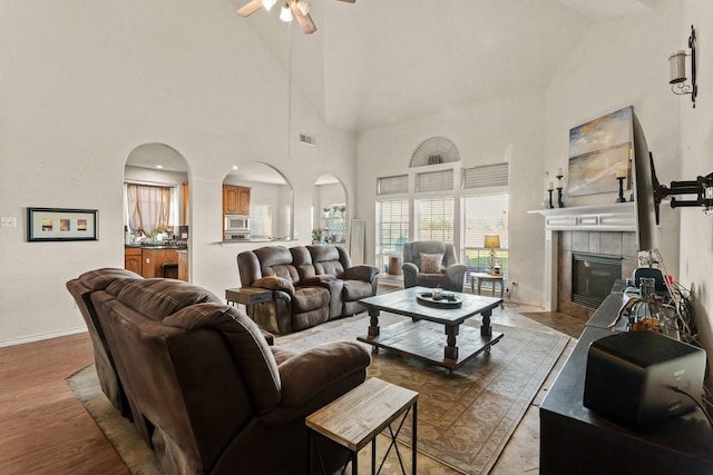 living area featuring ceiling fan, arched walkways, a fireplace, baseboards, and light wood-style floors