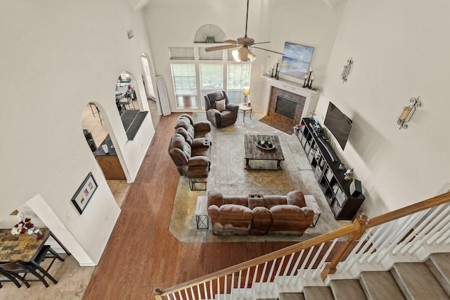 living area with a high ceiling, stairway, a tiled fireplace, and light wood-style flooring