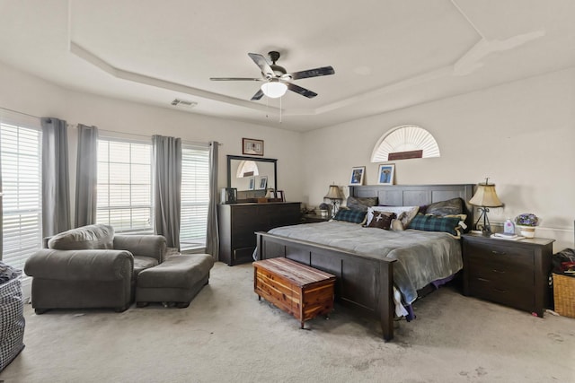 bedroom featuring a tray ceiling, visible vents, and light carpet