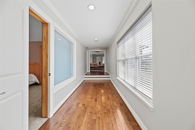 hall with light wood finished floors, ornamental molding, and baseboards