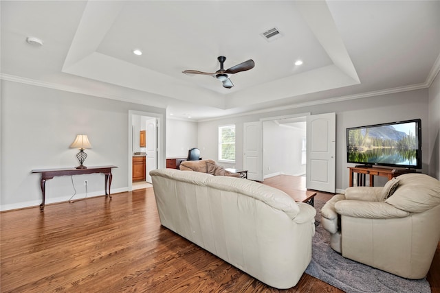 living room featuring a raised ceiling, visible vents, baseboards, and wood finished floors