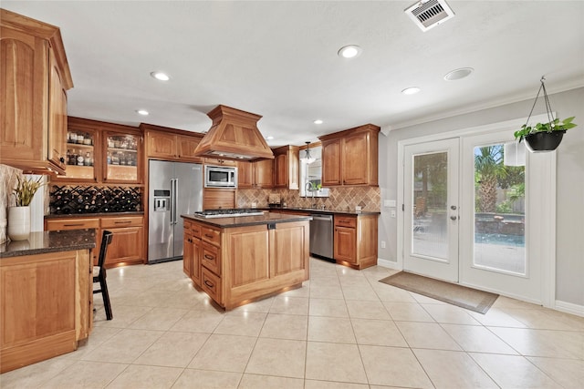 kitchen with island range hood, appliances with stainless steel finishes, a center island, dark stone countertops, and glass insert cabinets