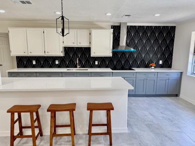 kitchen with wall chimney exhaust hood, hanging light fixtures, white cabinets, a sink, and a kitchen bar