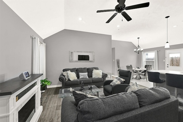 living room with lofted ceiling, ceiling fan with notable chandelier, a fireplace, wood finished floors, and baseboards