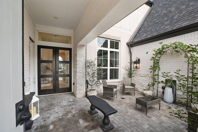 view of exterior entry featuring french doors, roof with shingles, a patio area, and brick siding