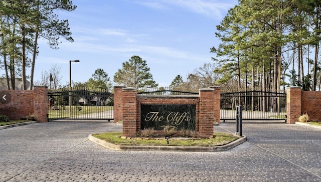 community sign with driveway, fence, and a gate