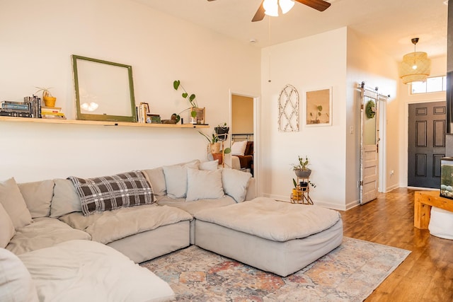 living area with a high ceiling, a barn door, ceiling fan, wood finished floors, and baseboards