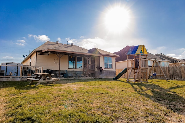 back of house featuring fence, a lawn, and a playground