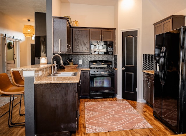 kitchen with dark brown cabinetry, a sink, black appliances, and a barn door