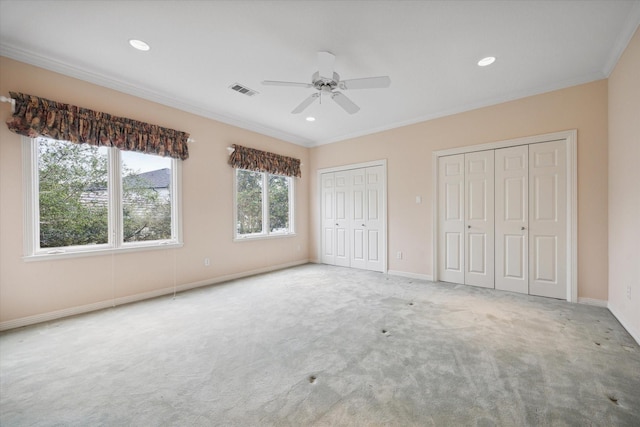 unfurnished bedroom with baseboards, visible vents, ornamental molding, carpet flooring, and multiple closets