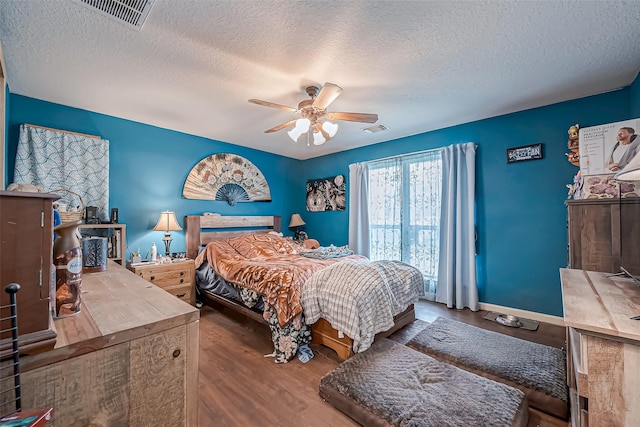 bedroom with a ceiling fan, visible vents, a textured ceiling, and wood finished floors