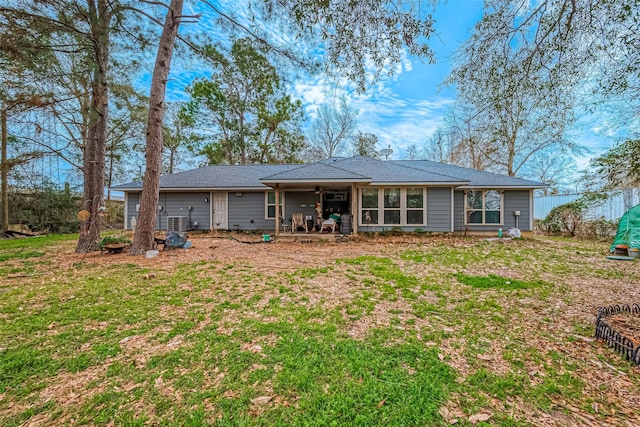 rear view of property with central air condition unit, fence, and a lawn