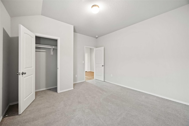 unfurnished bedroom with a closet, light carpet, vaulted ceiling, a textured ceiling, and baseboards