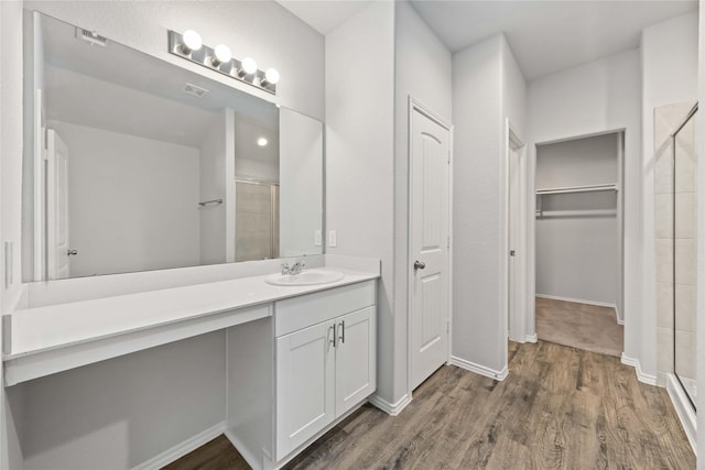 bathroom featuring a spacious closet, a stall shower, wood finished floors, and vanity