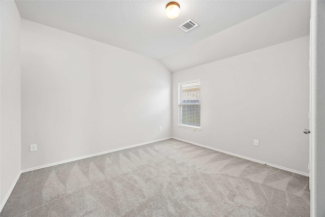 empty room with light colored carpet, visible vents, vaulted ceiling, and baseboards