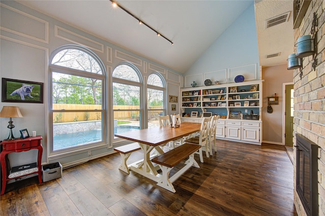 dining area featuring dark wood-style floors, a large fireplace, visible vents, and high vaulted ceiling