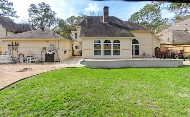 rear view of house with cooling unit, fence, a yard, a chimney, and a patio area