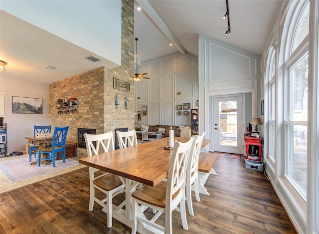 dining room featuring high vaulted ceiling, a fireplace, visible vents, beamed ceiling, and dark wood finished floors