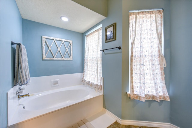 full bath featuring a garden tub, baseboards, and a textured ceiling