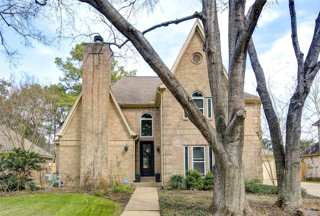 tudor house with brick siding, a chimney, and roof with shingles