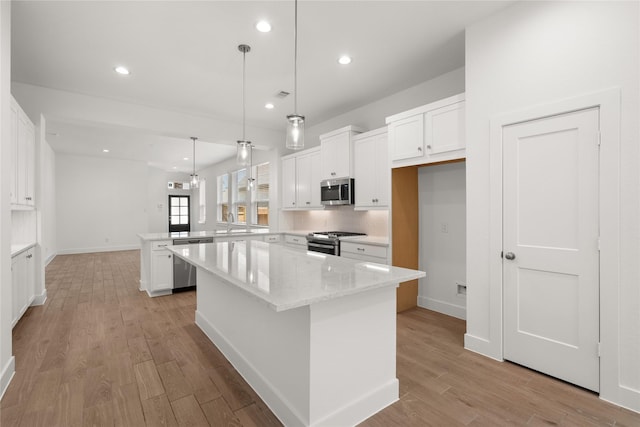 kitchen featuring white cabinets, a kitchen island, appliances with stainless steel finishes, light stone counters, and hanging light fixtures