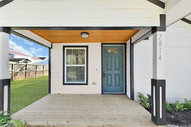 view of exterior entry with a deck, a lawn, and fence