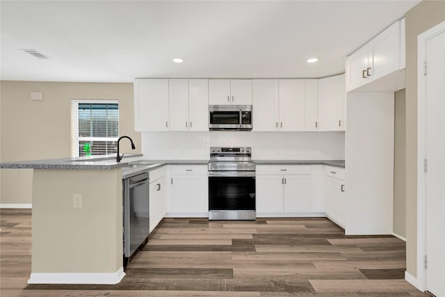 kitchen featuring stainless steel appliances, recessed lighting, white cabinetry, wood finished floors, and a peninsula