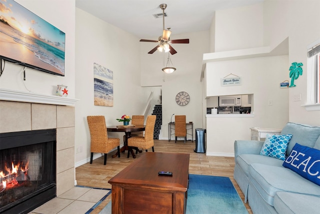 living room featuring baseboards, visible vents, a ceiling fan, and a tiled fireplace