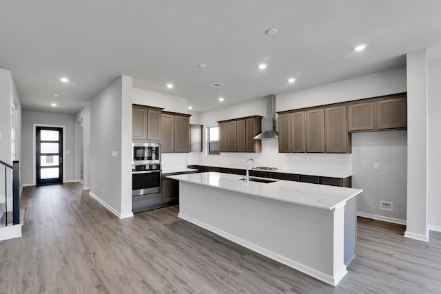 2920 Apple Rose, Katy, TX 77493 - kitchen featuring wall chimney range hood, light wood-type flooring, recessed lighting, stainless steel appliances, and a kitchen island with sink