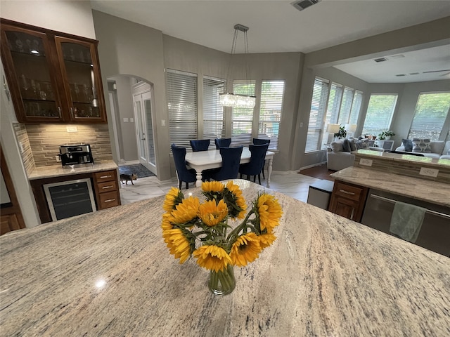 kitchen with arched walkways, glass insert cabinets, open floor plan, light stone countertops, and beverage cooler