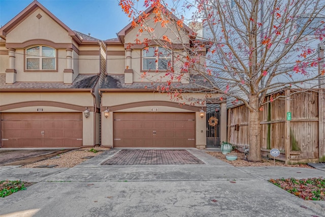 view of property featuring decorative driveway, stucco siding, a shingled roof, an attached garage, and fence