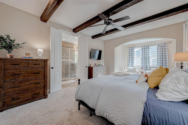 bedroom with a ceiling fan, light colored carpet, beamed ceiling, and ensuite bath