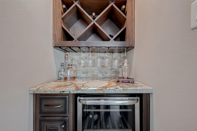 bar with beverage cooler, a textured wall, a dry bar, and tasteful backsplash