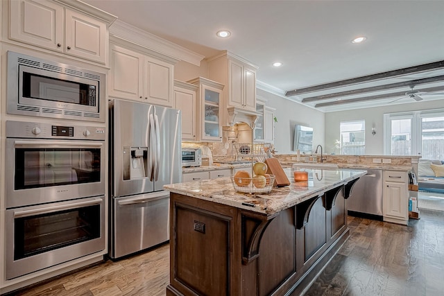 kitchen featuring glass insert cabinets, appliances with stainless steel finishes, a breakfast bar, light stone counters, and a center island