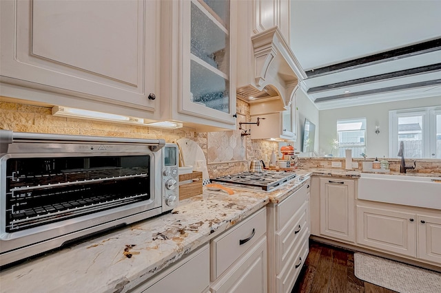 kitchen featuring light stone counters, a sink, glass insert cabinets, and decorative backsplash