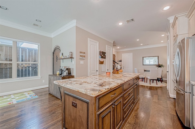 kitchen with wood finished floors, visible vents, a kitchen island, freestanding refrigerator, and brown cabinets