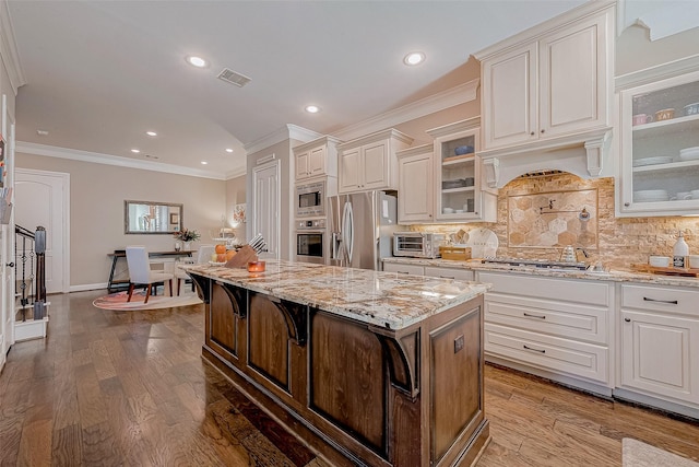 kitchen with visible vents, glass insert cabinets, a center island, stainless steel appliances, and a kitchen bar