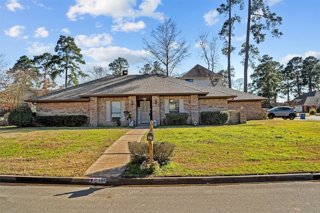 view of front of house with a shingled roof, a front lawn, and brick siding