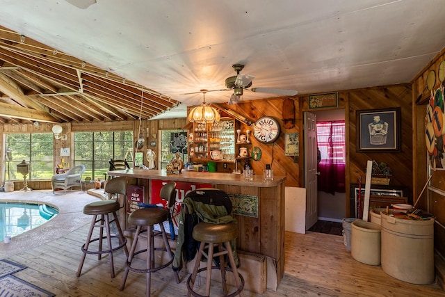 bar featuring a bar, wood walls, wood finished floors, and a ceiling fan