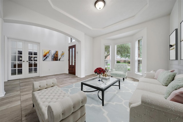 living room featuring light tile patterned floors, baseboards, arched walkways, a raised ceiling, and french doors