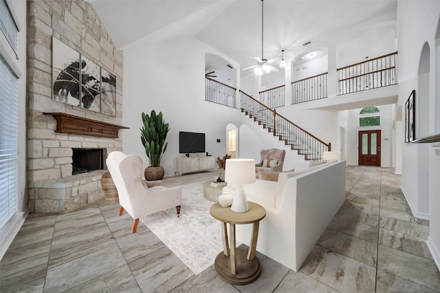 living room with marble finish floor, stairway, a towering ceiling, a ceiling fan, and a stone fireplace