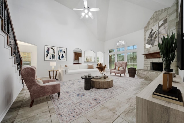 living area featuring arched walkways, ceiling fan, a stone fireplace, and stairs