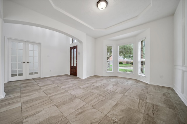 unfurnished room featuring baseboards, arched walkways, a raised ceiling, and french doors