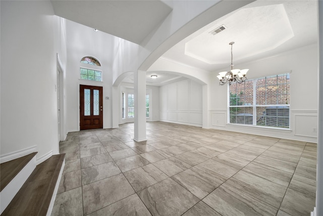 entryway featuring a chandelier, arched walkways, a decorative wall, visible vents, and a tray ceiling